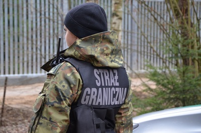 funkcjonariusz SG w kamizelce z napisem Straż Graniczna, bariera w tle 