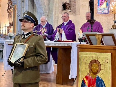 Funkcjonariusz trzyma portret en. bryg. Jana Kruszewskiego, w tle kapłani sprawujący mszę święta Funkcjonariusz trzyma portret en. bryg. Jana Kruszewskiego, w tle kapłani sprawujący mszę święta