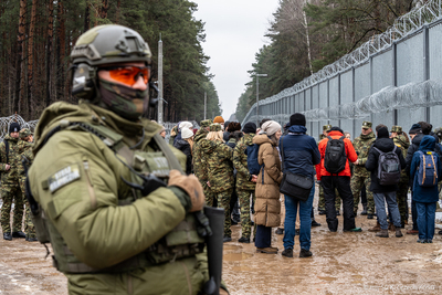 Funkcjonariusz Straży Granicznej w tle dziennikarze, funkcjonariusze SG i bariera na granicy polsko-białoruskiej Funkcjonariusz Straży Granicznej w tle dziennikarze, funkcjonariusze SG i bariera na granicy polsko-białoruskiej