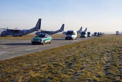 Pojazdy Straży Granicznej jadą, obok stoją samoloty transportowe Pojazdy Straży Granicznej jadą, obok stoją samoloty transportowe