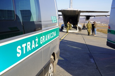 Pojazd Straży Granicznej za nim samolot transportowy z funkcjonariuszami SG eskortującymi cudzoziemców Pojazd Straży Granicznej za nim samolot transportowy z funkcjonariuszami SG eskortującymi cudzoziemców