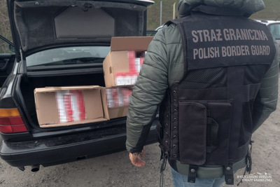 Funkcjonariusz Straży Granicznej stoi przy pojeździe, w którym widoczne są nielegalne papierosy Funkcjonariusz Straży Granicznej stoi przy pojeździe, w którym widoczne są nielegalne papierosy